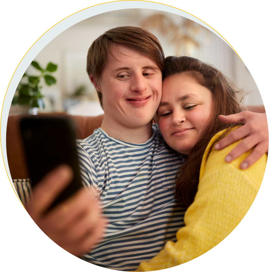 Young downs syndrome couple sitting on sofa using mobile phone to take selfie at home