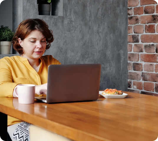 Close Up Picture of Woman in Yellow Crew Neck T-shirt Sitting on Desk is Focused Using her Laptop